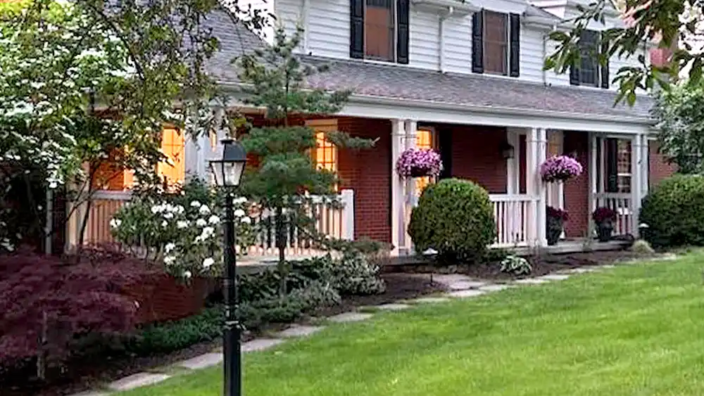 Front yard of red brick house with hanging annuals and manicured shrubs